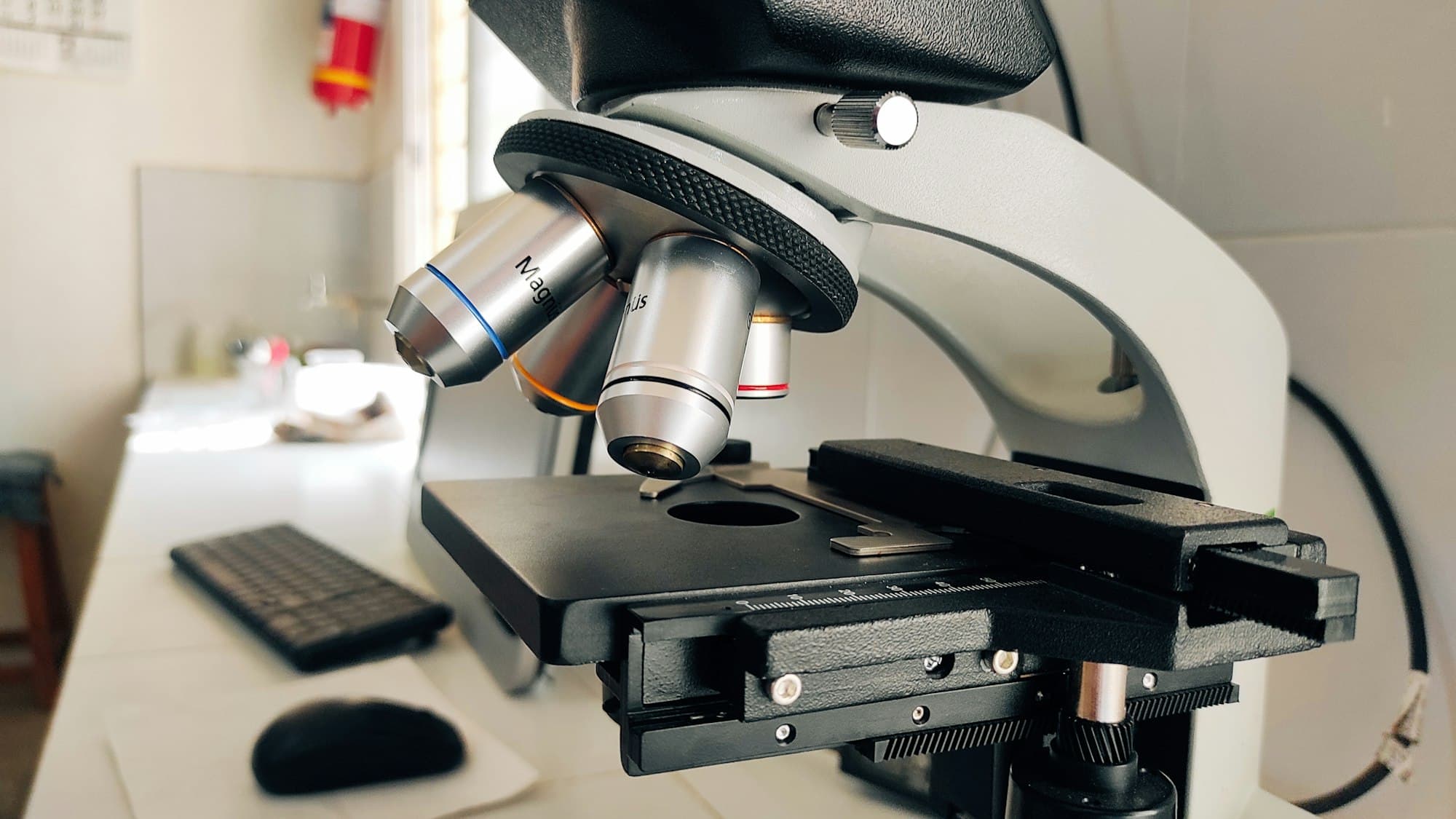 A laboratory microscope on a white bench beside a keyboard and mouse.