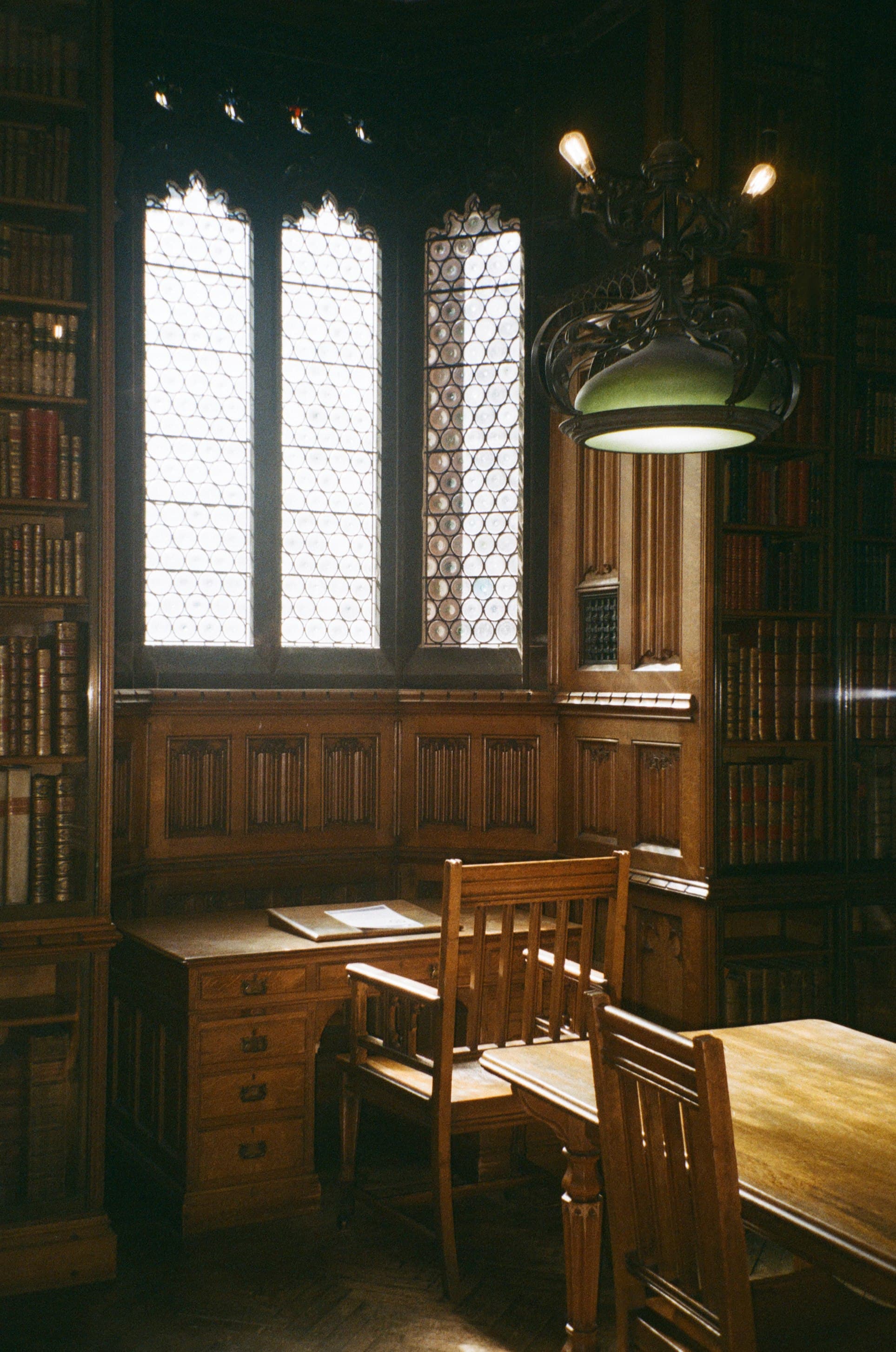 A wood-paneled library reading room with a desk, chairs, and leaded windows.
