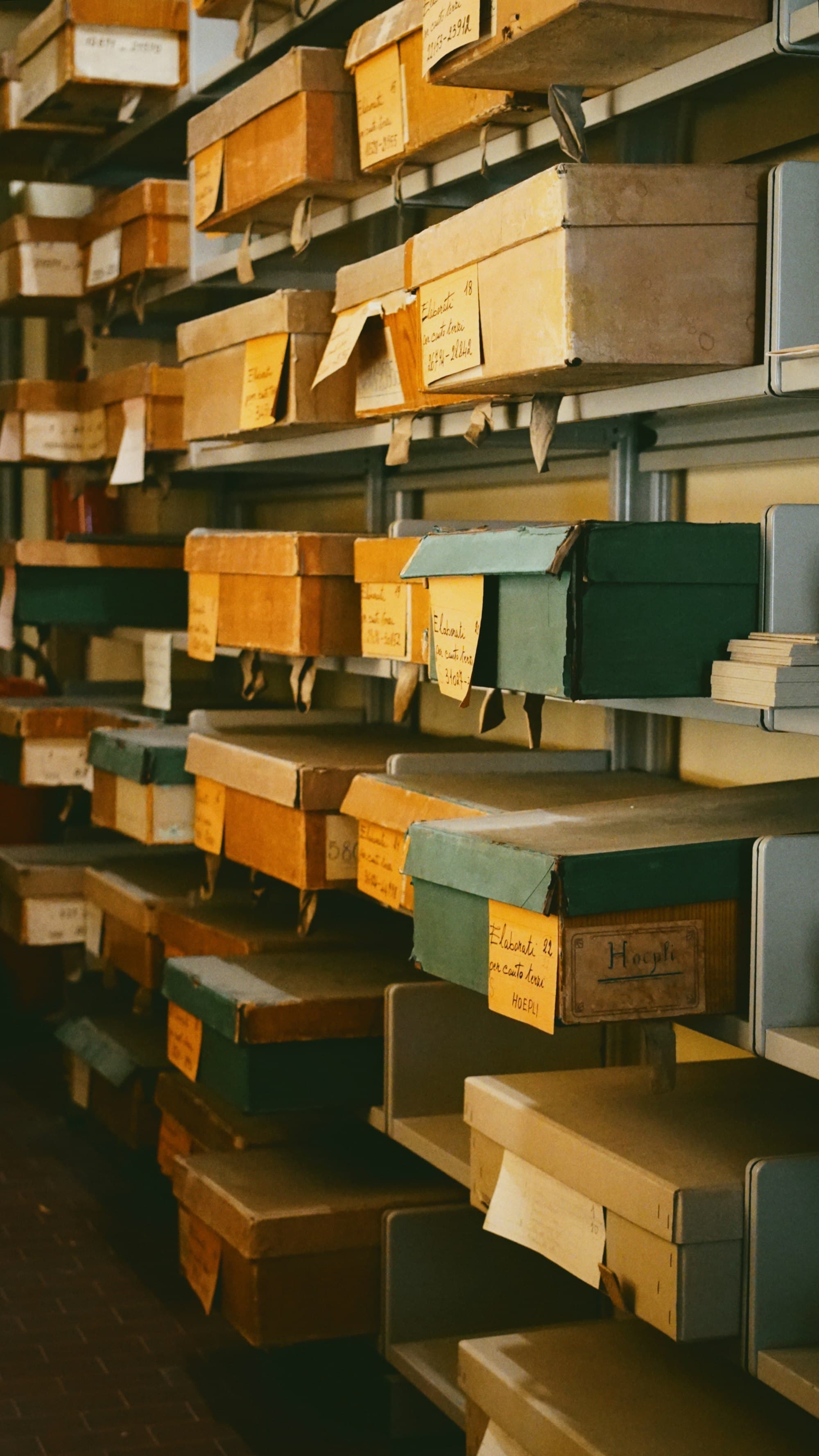 Archive shelves stacked with labeled cardboard document boxes in ochre, green, and grey.