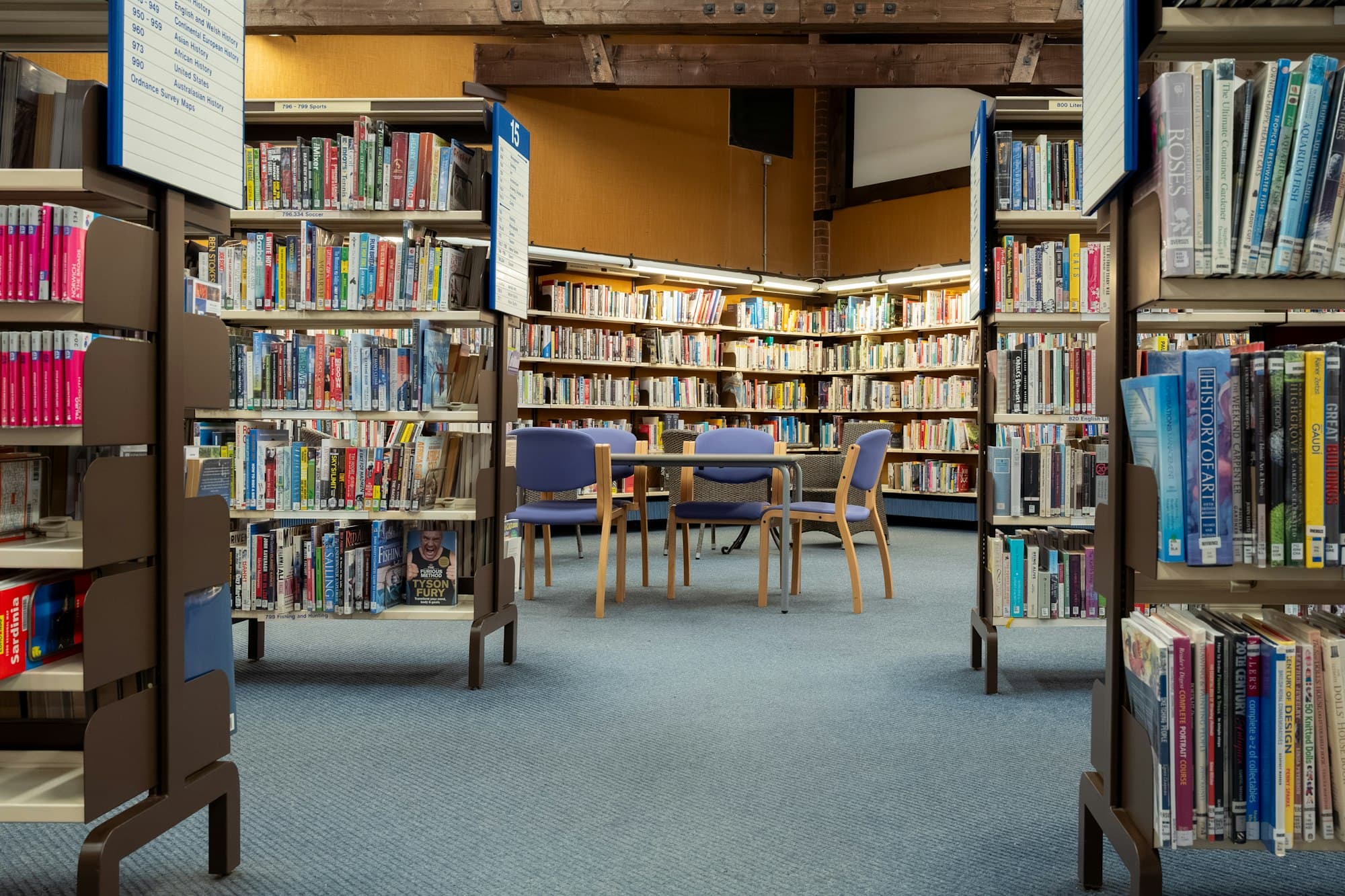 A bright public library with colorful shelves of books, blue chairs and reading tables.